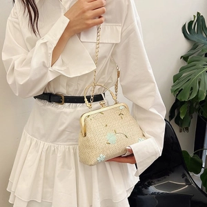 Detail of woven straw shoulder bag featuring blue floral embroidery and a gold metal handle