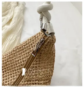 Detailed view of the beige straw hobo bag showing a smooth metal zipper and knot strap