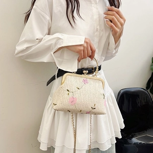 Detail of cream woven handbag featuring pink floral embroidery and a gold ring handle