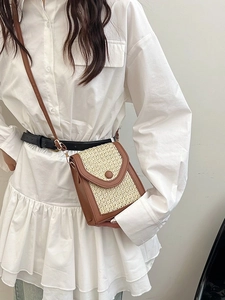 Mini straw woven crossbody bag with brown faux leather trim worn by model in white shirt