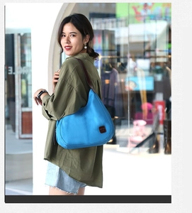 Sac hobo en toile bleue avec large bandoulière en cuir porté à l'épaule en ville