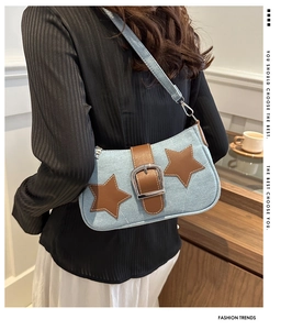 Detail of a denim shoulder bag with leather stars and chain worn by a model