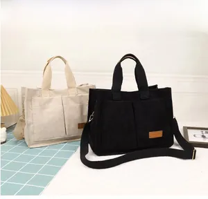Detail view of corduroy tote bags with front pockets and fashion label in beige and black