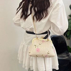 Detail of woven straw crossbody bag with floral embroidery and gold metal chain strap