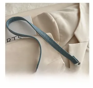 Detail of denim shoulder bag with leather reinforcement and metallic hook on beige blazer