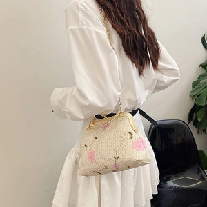 Detail of woven straw bag featuring delicate pink floral embroidery and gold chain strap