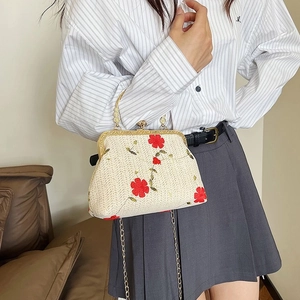 Detail of woven chain bag featuring red floral embroidery and golden metal clasp handle