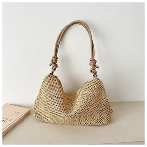 Minimalist straw shoulder bag with light brown leather knotted strap on a desk