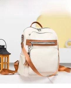 Detail of off-white canvas backpack with brown leather trim, tassels and zipper pockets