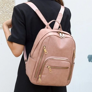 Rear view of a model wearing a pink faux leather backpack with gold metal zippers