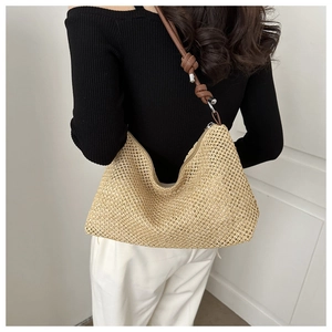 Detail of hand-woven straw hobo bag with brown leather shoulder strap and knot design