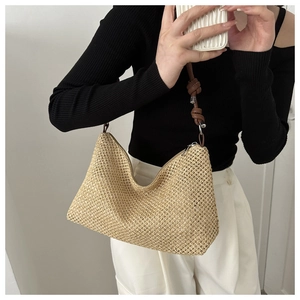 Detail of hand-woven straw tote bag featuring brown leather strap with knot and metal buckle