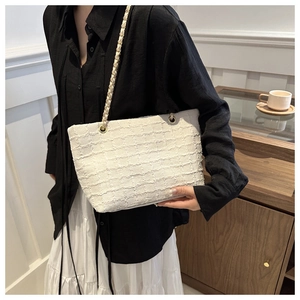 Detail of white tweed tote bag with gold chain strap worn by model in casual setting