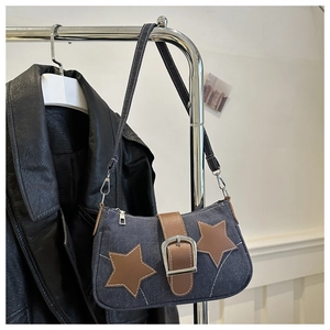 Detail view of a denim underarm bag featuring star patches and a brown leather buckle strap