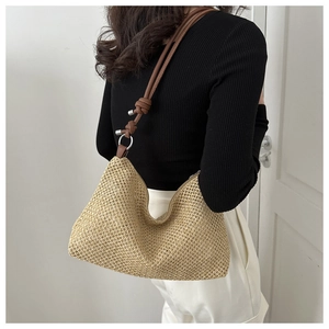 Straw hobo bag with knotted brown leather strap detail shown on a model against a white wall