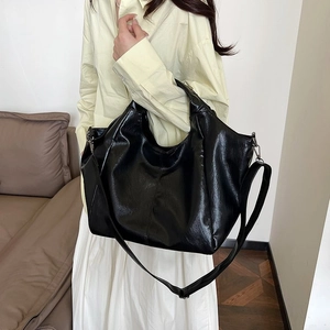 Close-up of black oversized hobo bag showing glossy textured leather and dual strap system