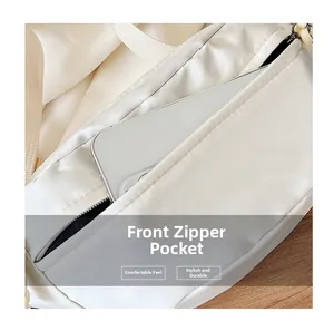 Detail of front zipper pocket on white crossbody bag holding a smartphone for scale