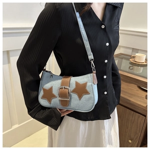 Close-up of light blue denim shoulder bag with brown star patches and metal buckle detail