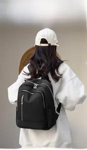 Rear view of model wearing a black waterproof nylon backpack with multiple silver zippers