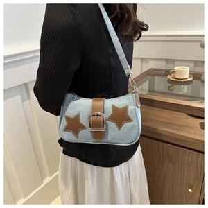 Detail of denim shoulder bag featuring star patches and leather strap with silver buckle