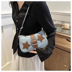 Detail of blue denim shoulder bag featuring leather star patches and metal buckle