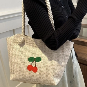 Sac cabas tissé en paille avec broderie cerise et poignées en corde porté par un mannequin