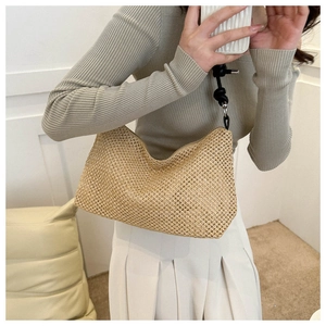 Detail of woven straw shoulder bag featuring black rope knot handle and silver hardware