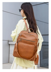 Detail view of brown PU leather backpack with multi-zipper pockets and side pocket on model