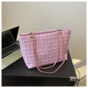 Close-up of pink textured tote bag with chain strap next to a laptop on a desk