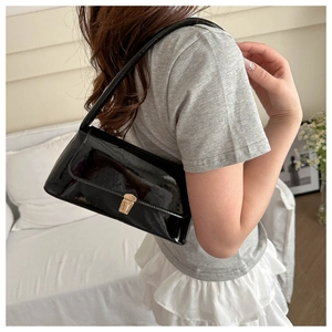 Detail of a black patent leather underarm bag with a golden square metal clasp on a model