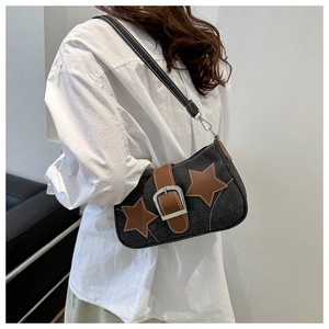 Detail view of denim shoulder bag featuring leather star patches and silver metal buckle