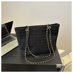 Detailed view of black quilted tote bag texture with metal chain straps on wooden surface