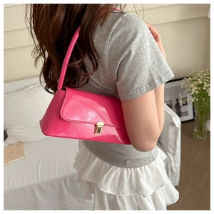 Detail of glossy hot pink underarm bag featuring a metallic gold twist-lock and slim strap