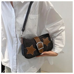 Detail of denim shoulder bag with leather star patches and metal buckle strap accents