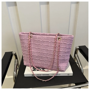 Detailed shot of pink tote bag with pleated texture and gold chain strap on books