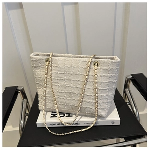 Close-up of cream white tweed tote bag with woven texture and luxury metal chain strap