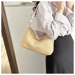 Close-up of woven straw shoulder bag featuring decorative white rope knot strap detail