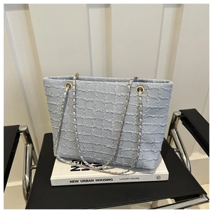 Detail view of a light blue woven tote bag with chain strap resting on books