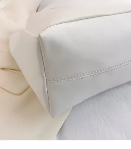 Detail of neat stitching on the bottom edge of a cream faux leather tote bag