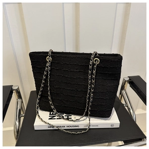 Detail of black textured pleated fabric and gold chain strap on a stylish tote bag