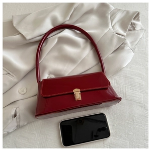 Detail view of burgundy patent leather baguette bag with a gold clasp on silk fabric
