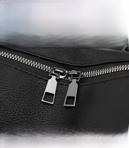 Macro shot of smooth gunmetal zippers and lychee grain leather texture on a backpack