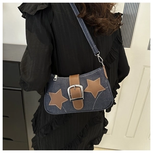 Detail of denim shoulder bag featuring brown star patches and metal chain accents