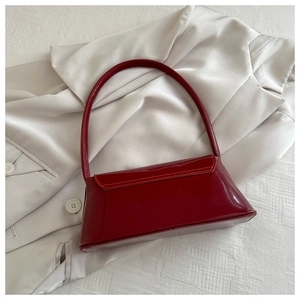 Close-up of glossy deep red patent leather underarm bag on elegant white fabric