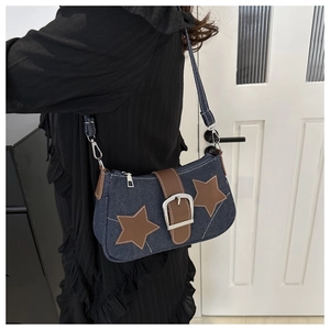 Detail of denim underarm bag with leather star patches and silver buckle on model