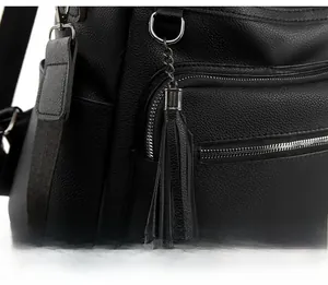 Detailed close-up of black litchi grain leather backpack with silver zippers and tassels