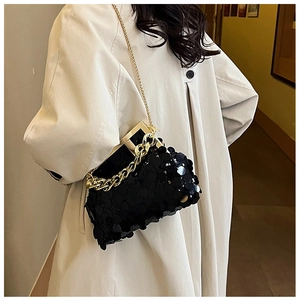 Close-up of black sequin evening bag with gold chain strap on beige trench coat