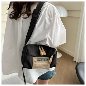 Detailweergave van de zwarte oxford crossbody tas met logo patch en bruine ritstrekkers