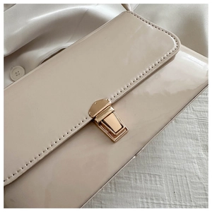 Close-up of beige patent leather bag featuring a glossy finish and gold metal buckle