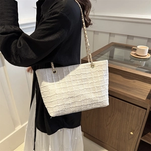 Elegant white tweed tote bag with metal chain strap worn by a model in a cozy interior